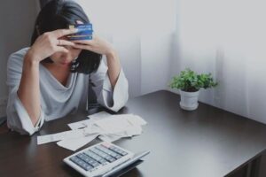 (woman stressed over finances holding a credit card to her head)