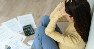(Stressed woman sitting on the floor with overdue bills and a calculator, representing the emotional toll of overwhelming credit card debt.)